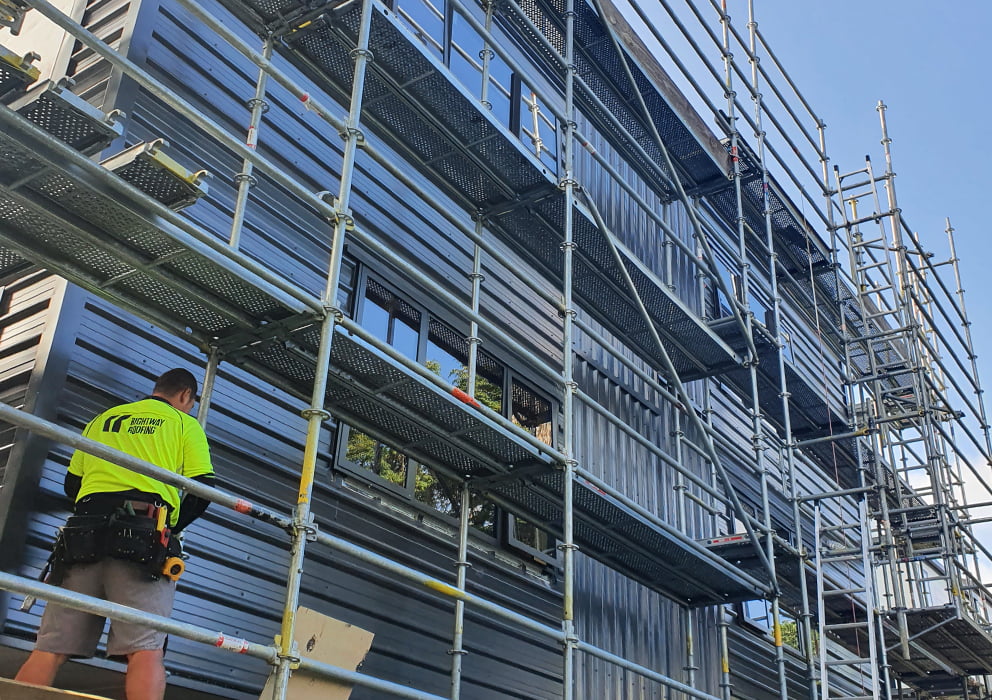 A building development with steel cladding and builders on scaffolding.