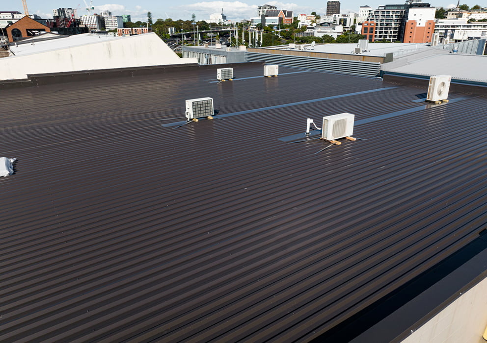 A new commercial roof replacement with black long run roofing and air conditioning units.
