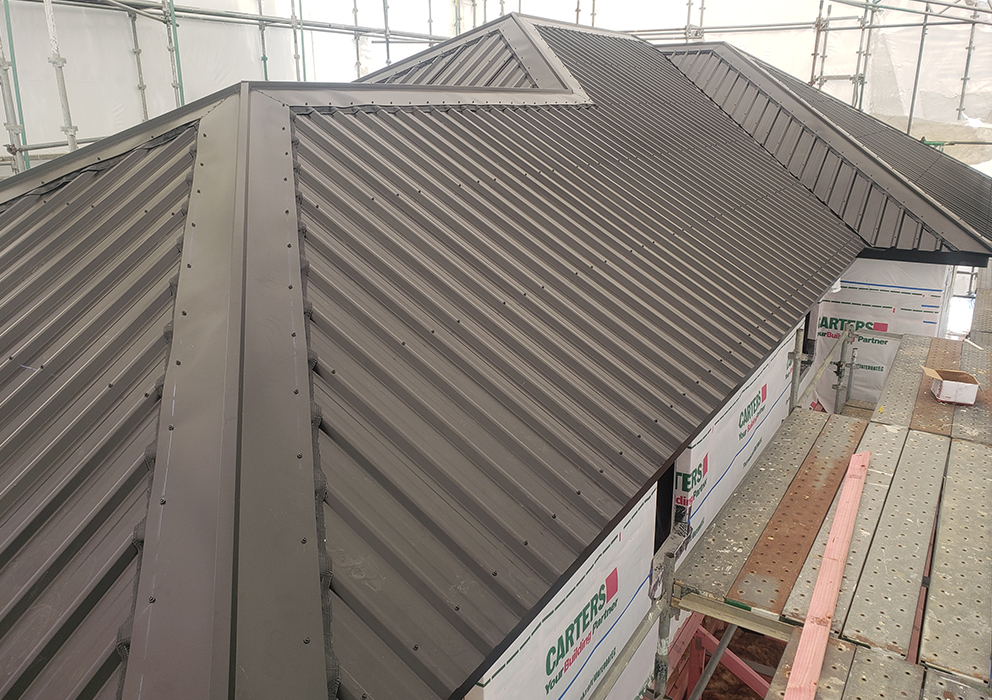 A grey long run roof being installed on a new build at a builders yard.