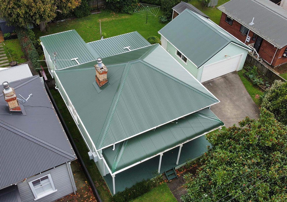 An aerial view of a villa with a green long run roof replacement.